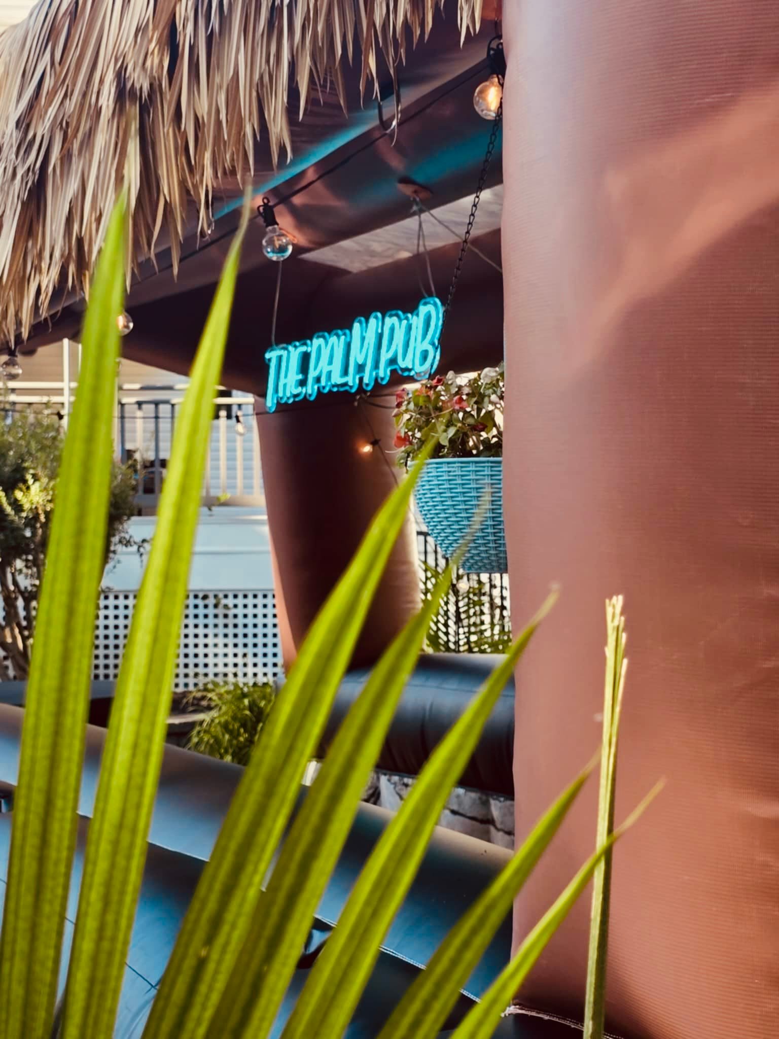 The Palm Pub neon sign glowing through tropical palm leaves
